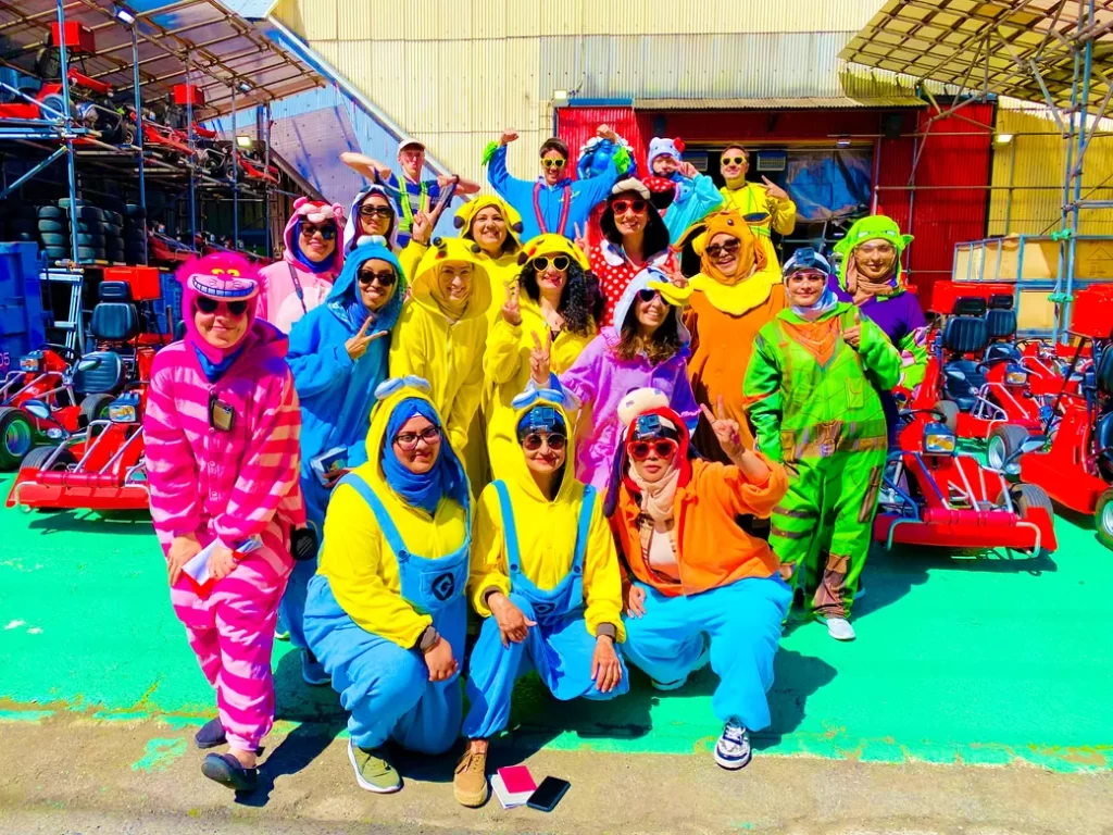IMG_0643 - StreetKart Group photo of people in colorful onesies posing at a go-kart track, with karts lined up in the background.
